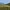 Castle atop a green hill overlooking vineyards and distant mountains under a clear sky.