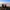 Two people sit on a grassy hilltop taking photos of clouds at sunrise.