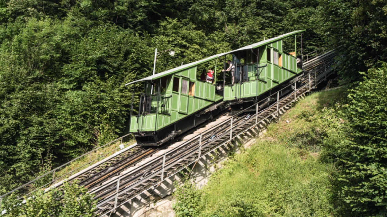 Aerial view of a historic cityscape featuring intricate rooftops and Gothic architectural details, with a person standing on a balcony.