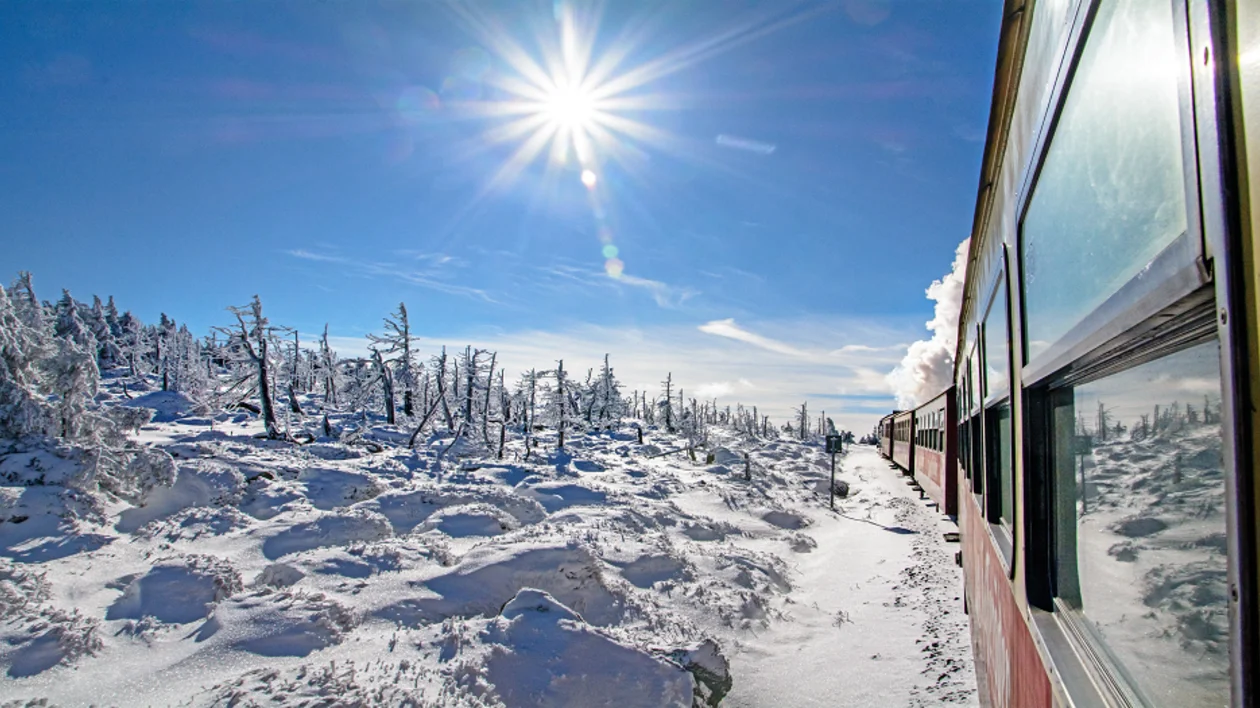 A railroad with a steam locomotive in the snow on a sunny day.