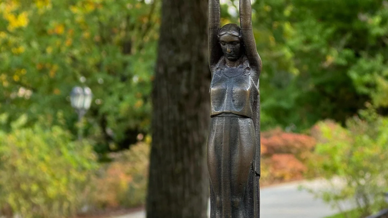 A iron statue holding a star aloft in a park with autumn trees.