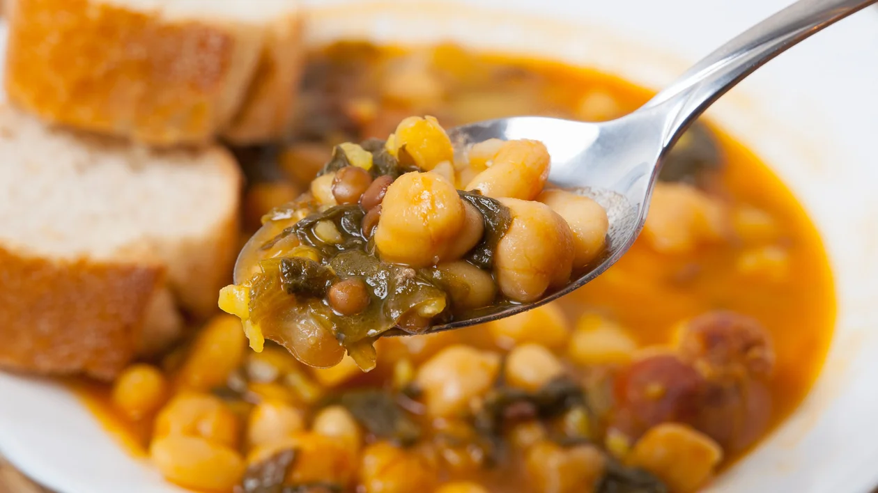 A hearty spoonful of traditional Spanish chickpea stew, rich with garbanzos and spinach, served alongside fresh, crusty bread. This comforting dish captures the essence of rustic, homemade Spanish cuisine.