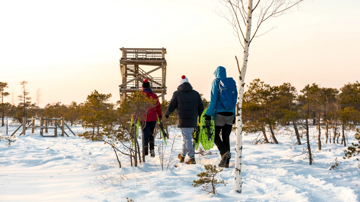 Group walking towards a wooden tower in a snowy landscape at sunset.