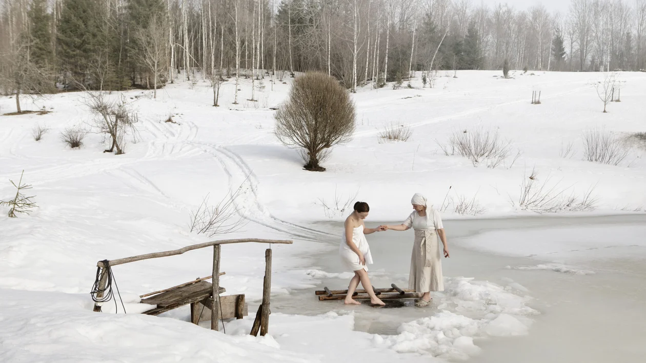 Two women entering in a traditional sauna ritual. On the background, a snow-covered landscape.