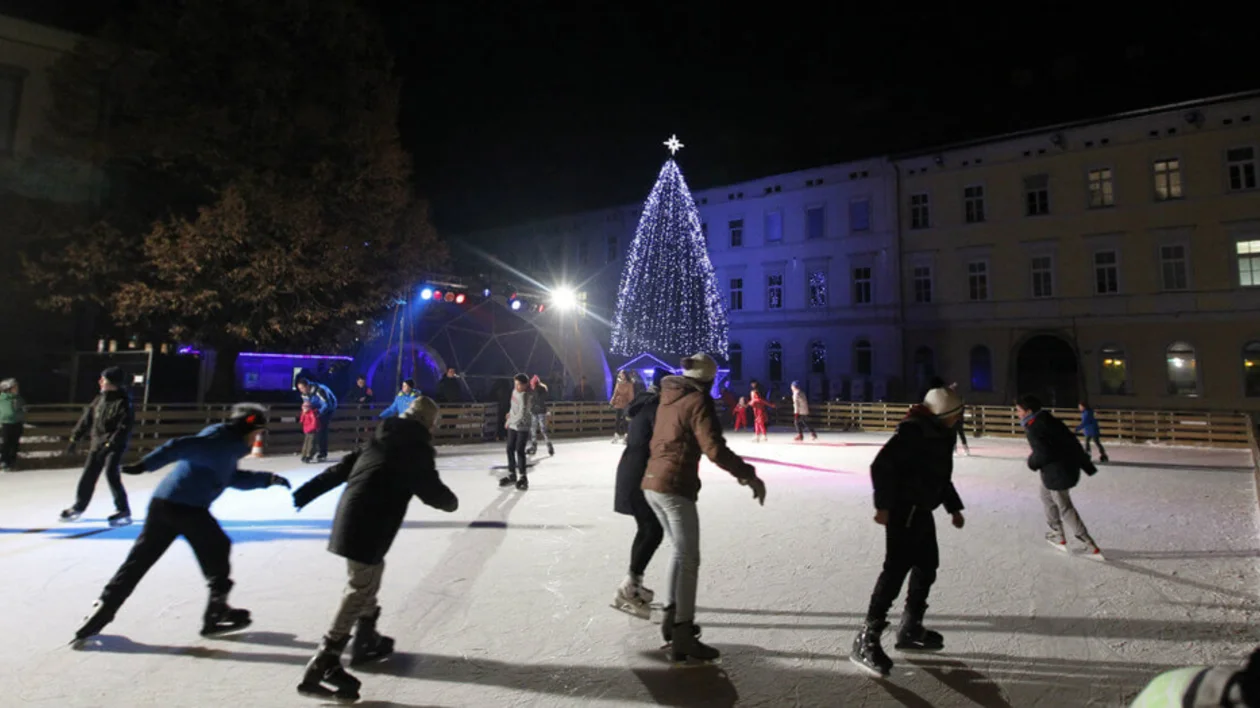 People ice skating at night with a lit Christmas tree in the background.