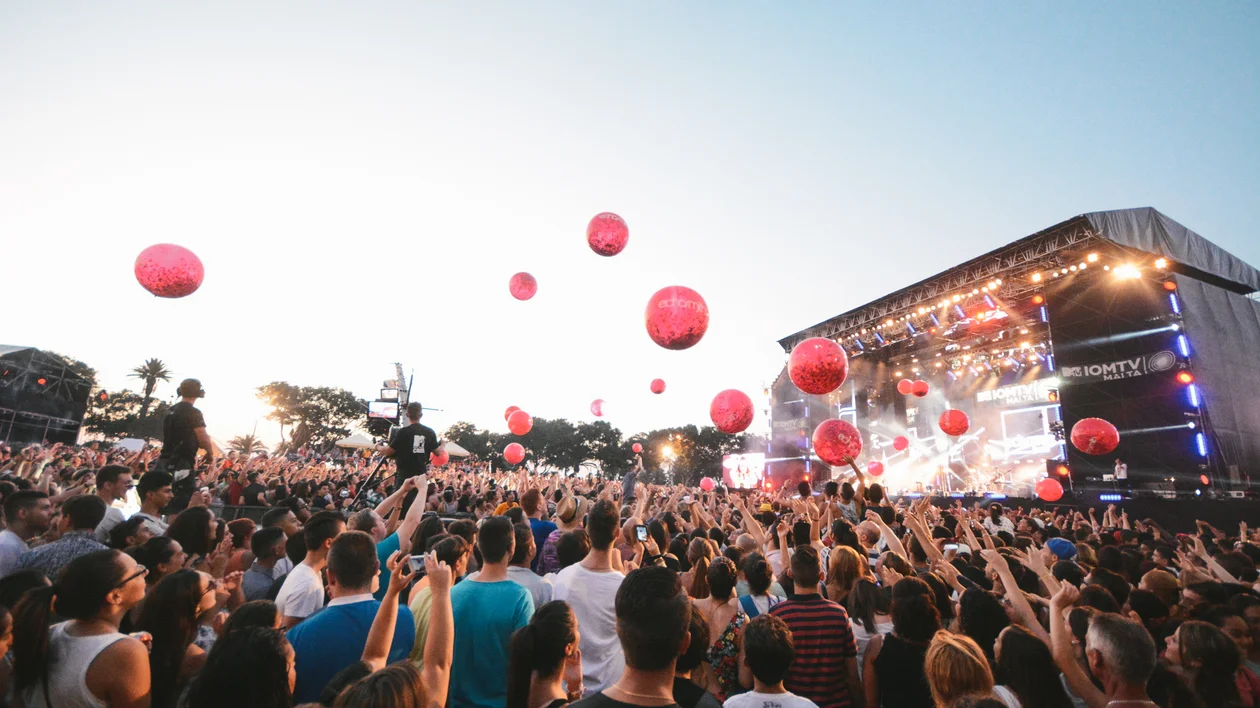 Crowd at the outdoor festival Isle of MTV in Malta with red balloons in the air and a lit stage in the background.
