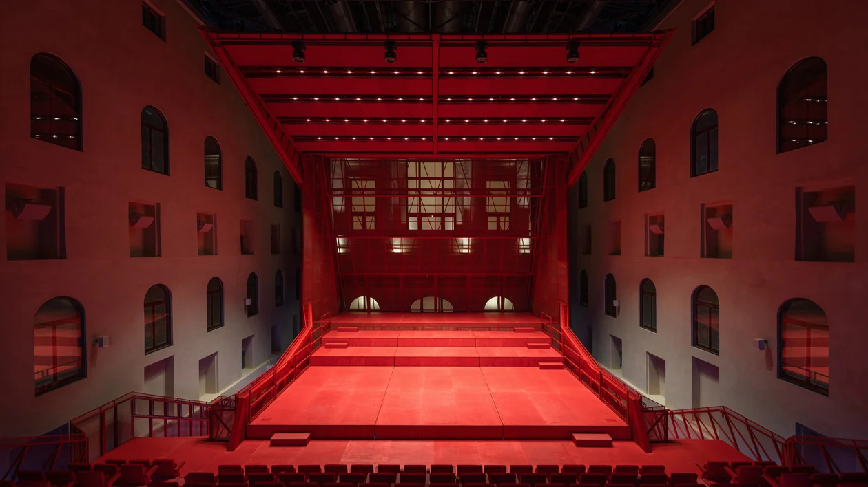 A red stage with seats in front of it, located inside the hall of a building.