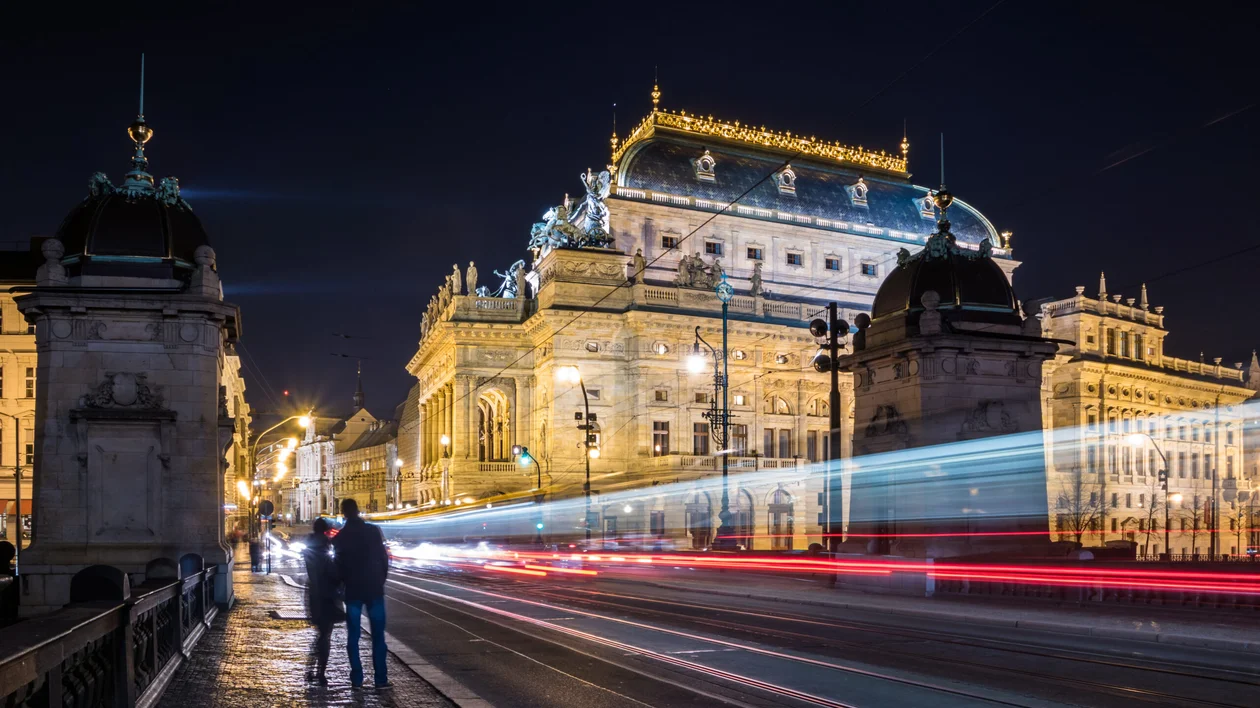 The illuminated National Theatre in Prague at night with light trails from passing vehicles.