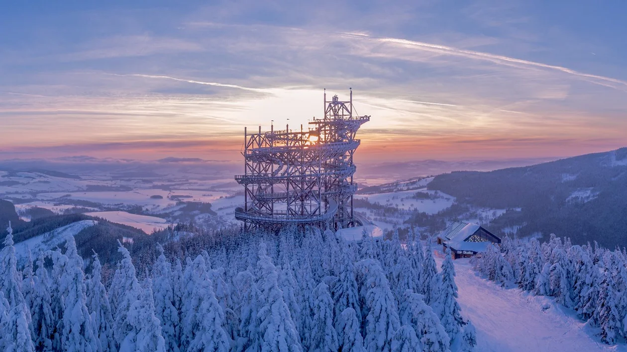 Panoramic view of a snowy landscape at sunset with an intricate observation tower.