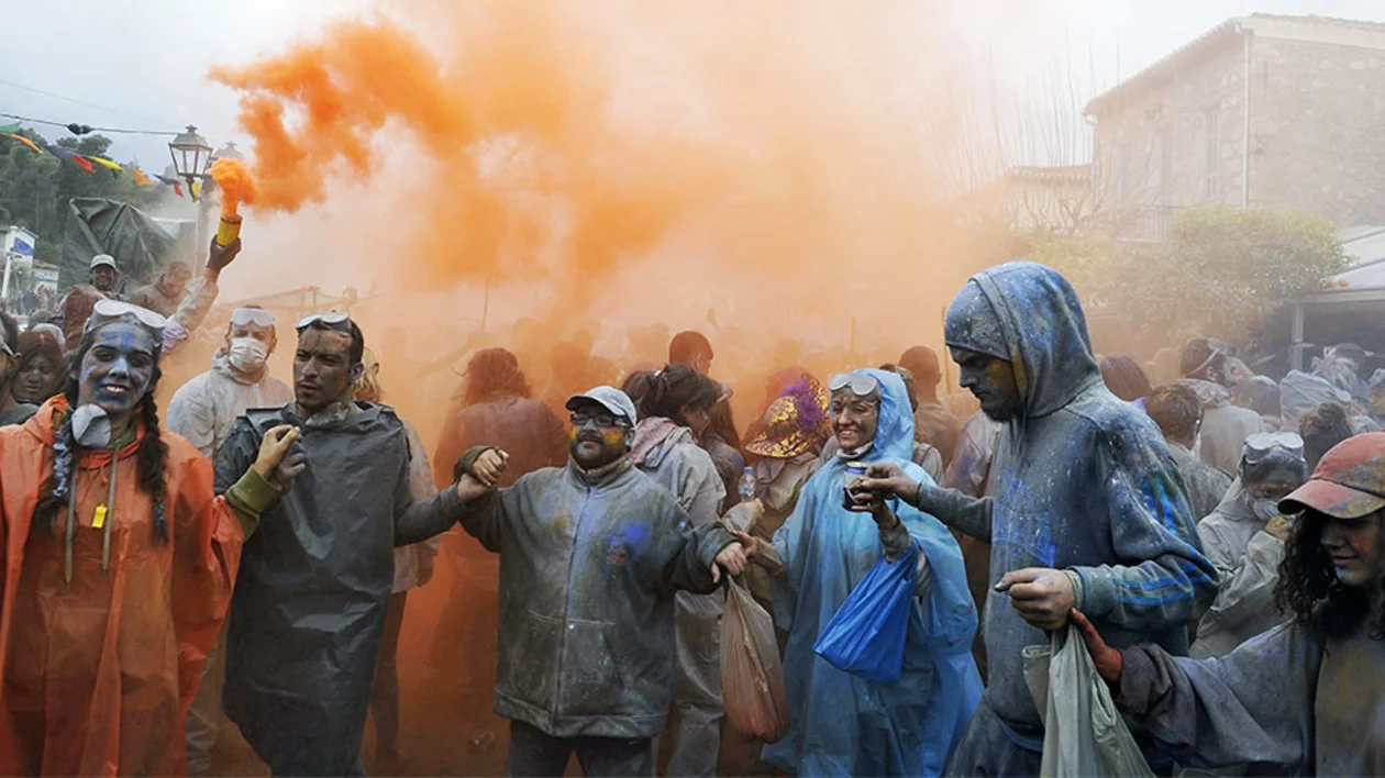 A crowd in protective gear surrounded by orange smoke in the flour war at Galaxidi, Greece.