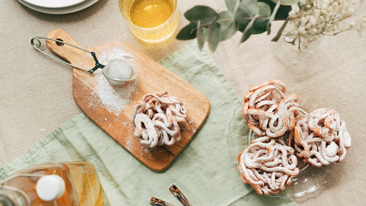 Freshly made funnel cakes dusted with powdered sugar on a wooden board and glass plate, rustic table setting.