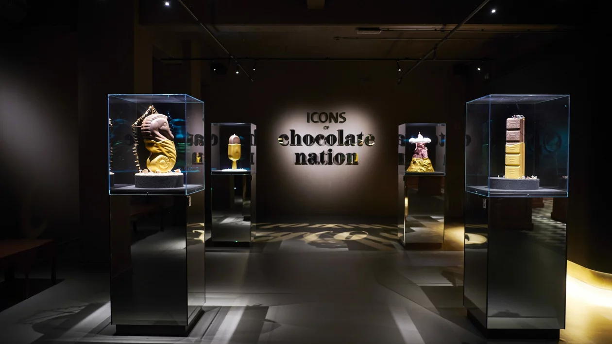 An exhibit featuring intricate chocolate sculptures under glass displays, with "Icons of Chocolate Nation" prominently showcased on the wall.