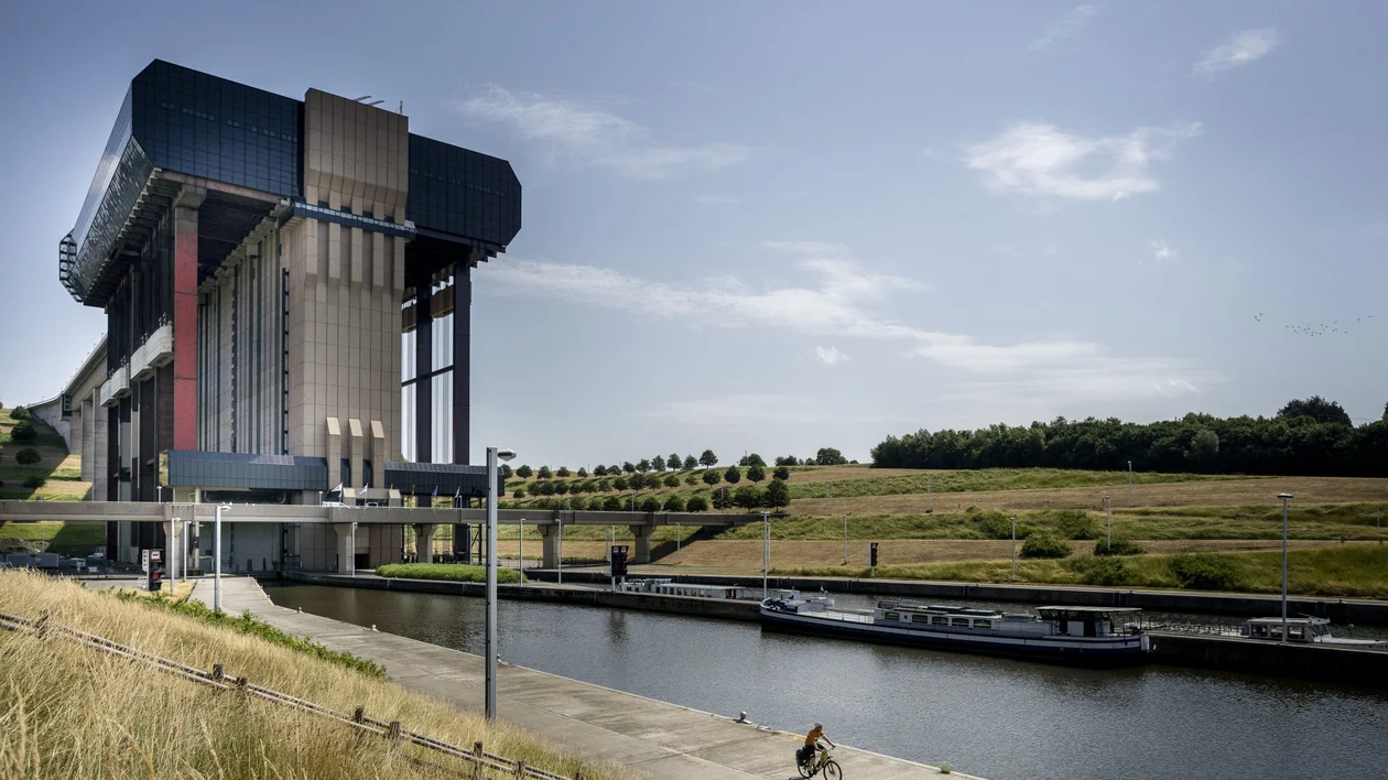 A cyclist rides along a canal near the impressive Strépy-Thieu boat lift under a clear sky.