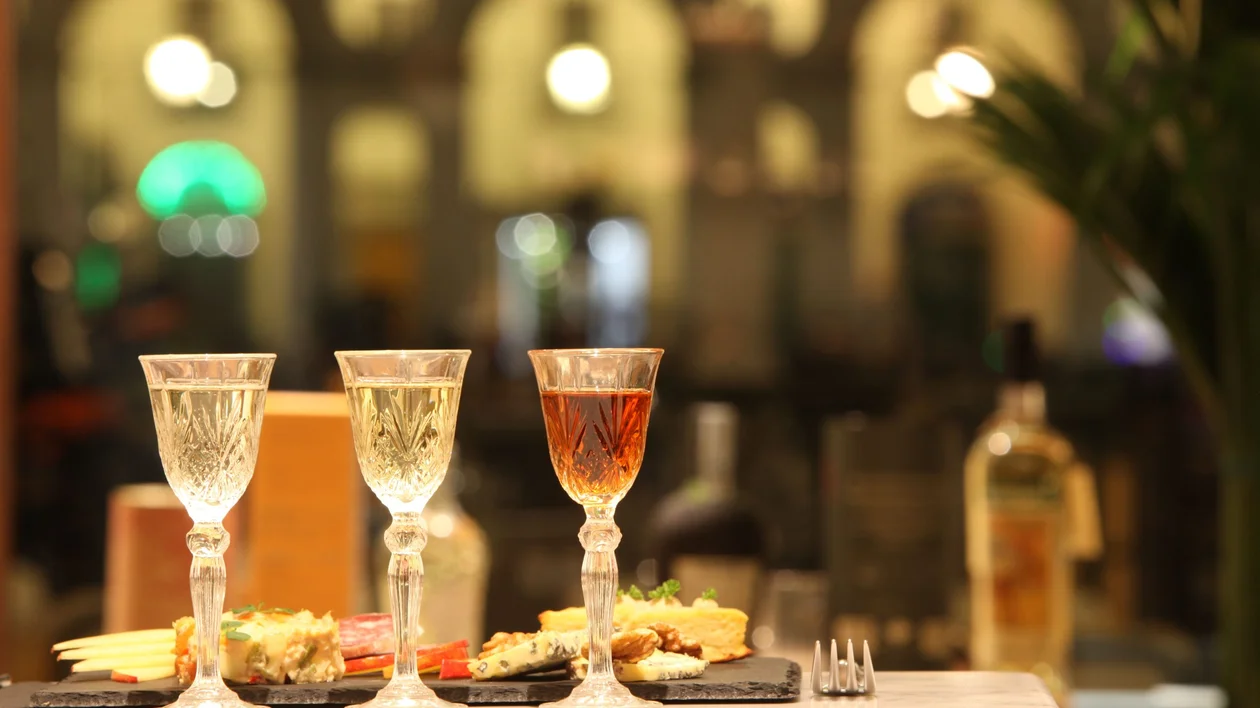 Three elegant crystal glasses filled with colorful drinks sit on a marble table, accompanied by gourmet appetizers in a softly lit venue.