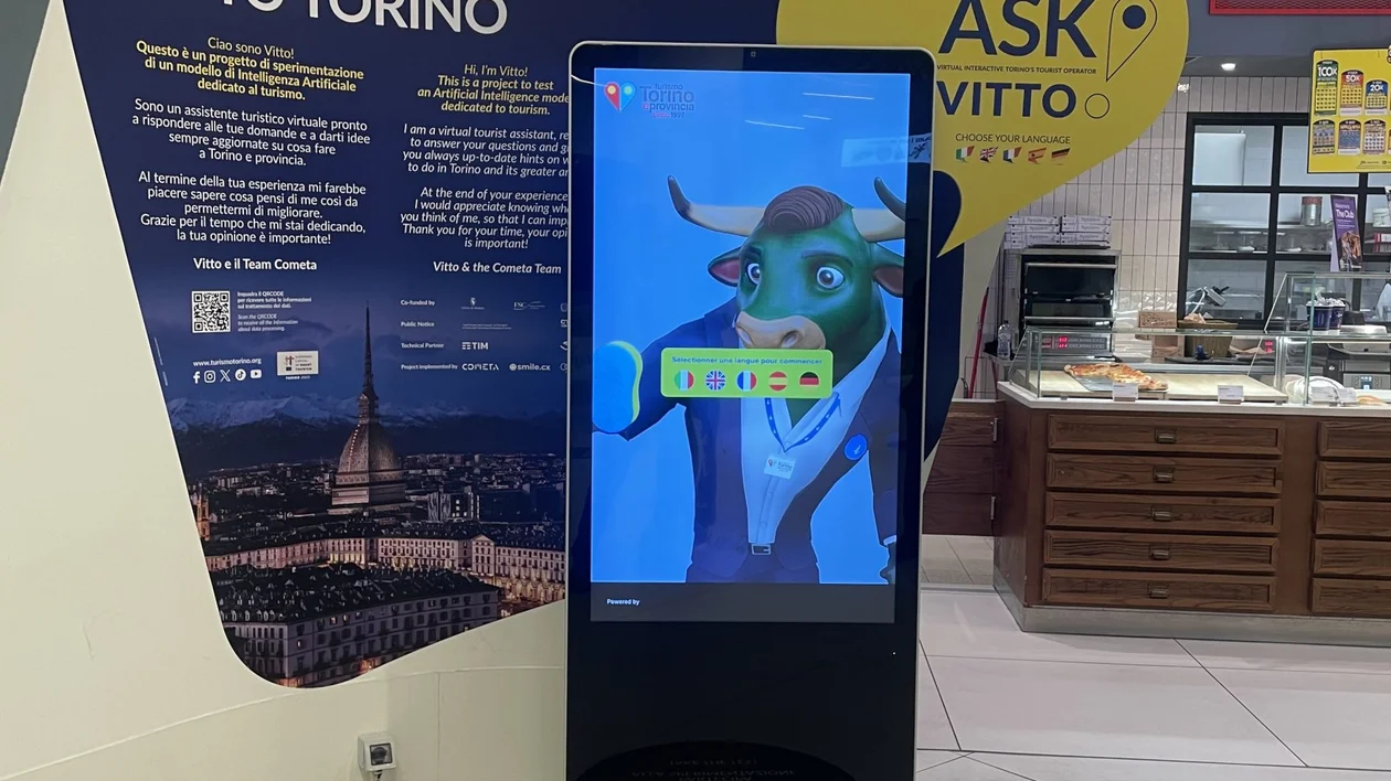 A digital kiosk in a welcoming space displaying "Ask Vitto," an interactive virtual assistant for tourists in Turin.