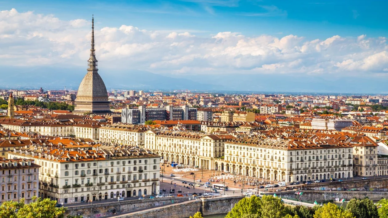 A panoramic view of Turin featuring the iconic Mole Antonelliana, overlooking historic buildings and the Po River beneath a blue sky.