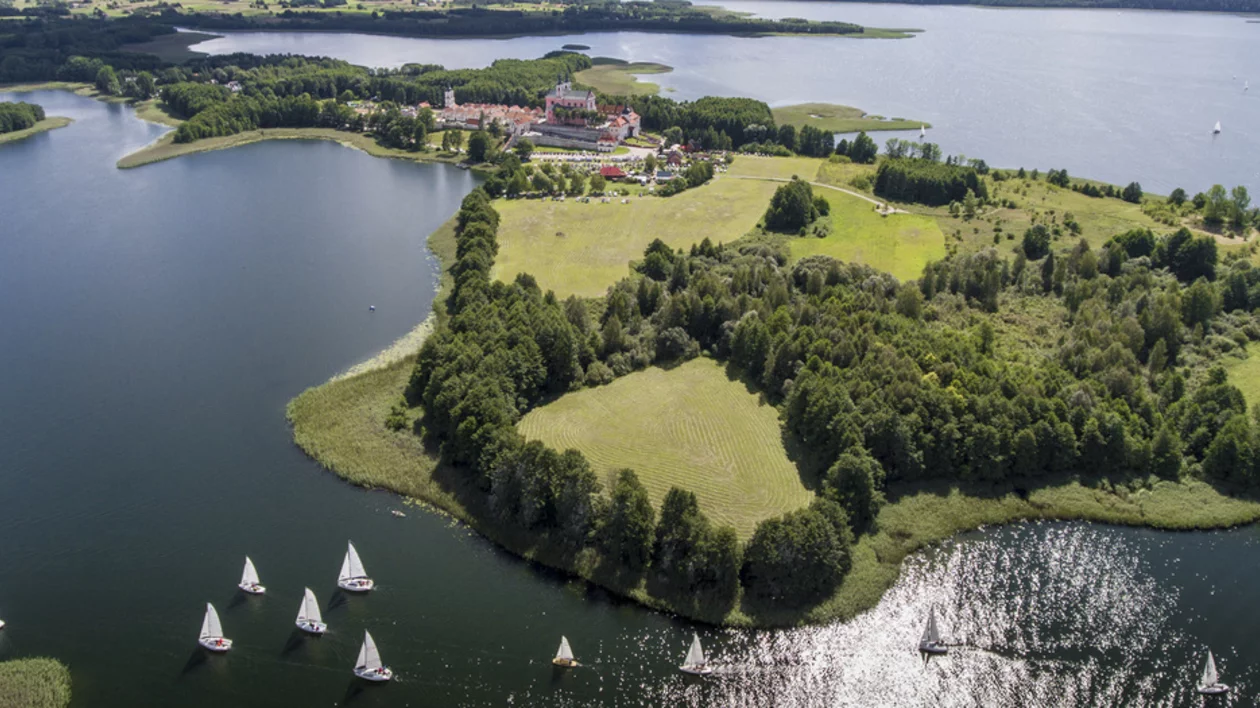 Aerial view of a serene lake surrounded by lush greenery, with a charming village and sailboats gliding across the water.