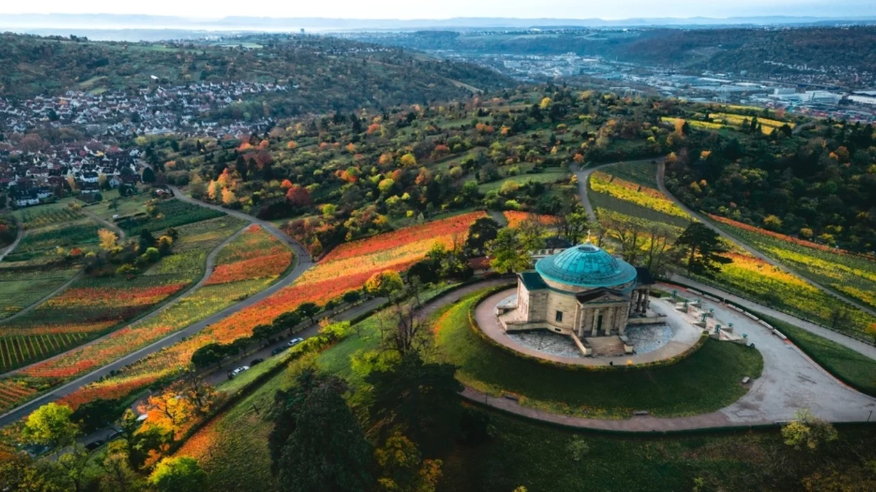 Aerial view of a scenic landscape featuring vibrant autumn vineyards, a historic gazebo, and a charming town in the distance.