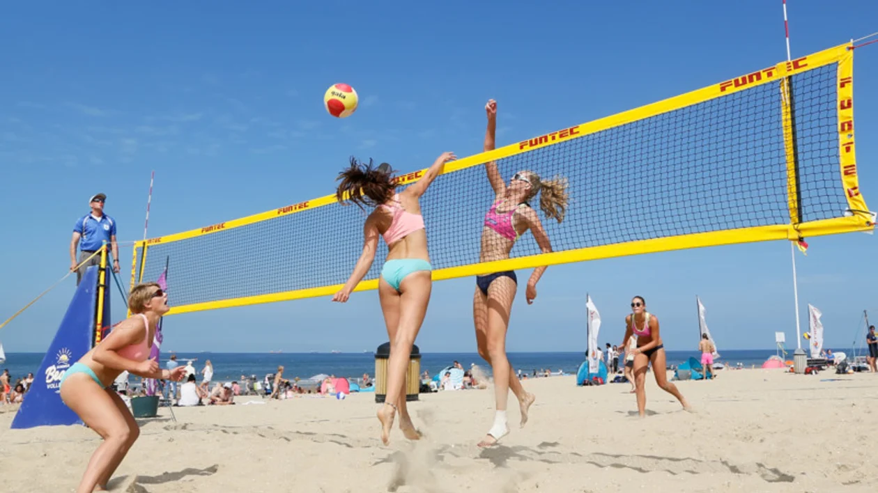 Women playing an energetic game of beach volleyball on a sandy beach with a clear blue sky in Scheveningen, Netherlands.