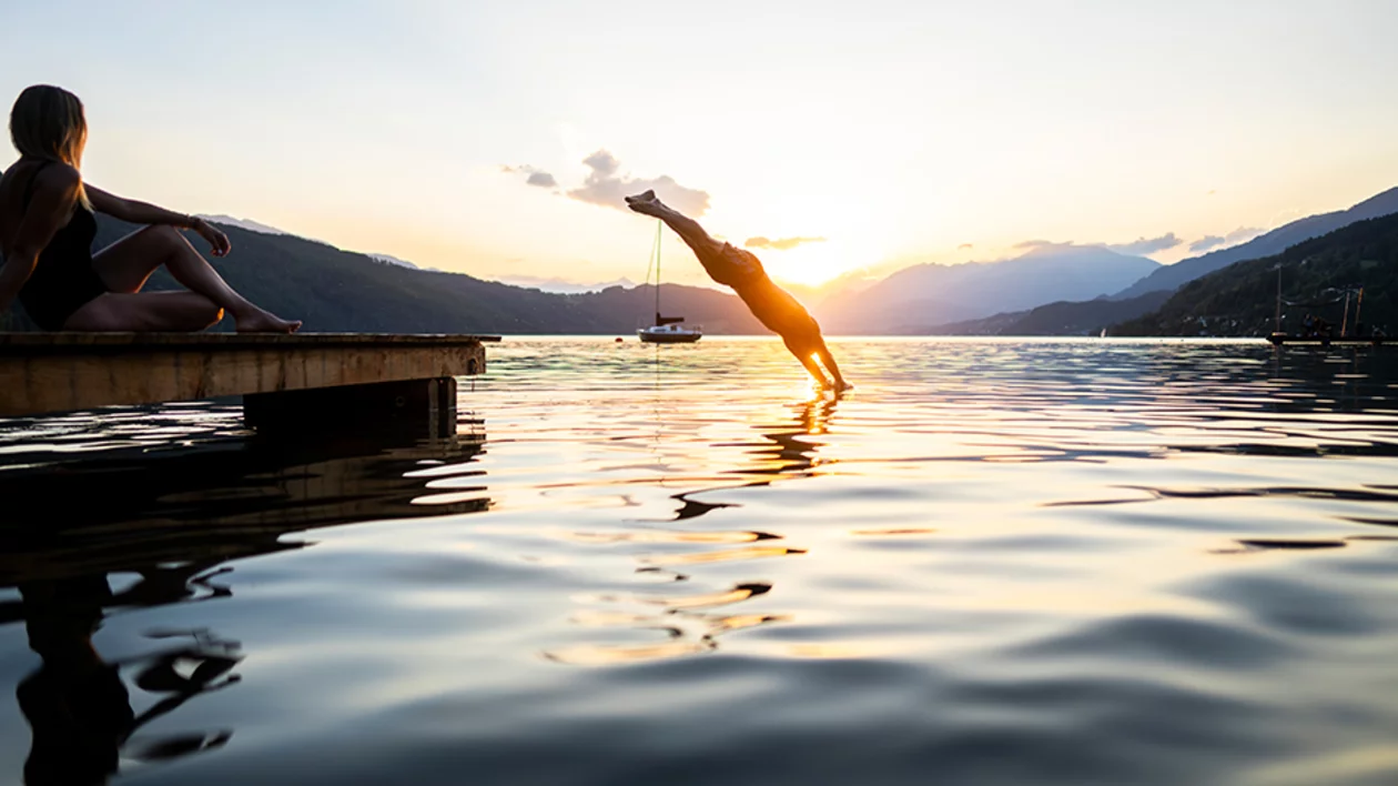 Man diving into a lake at sunset with mountains in the distance.
