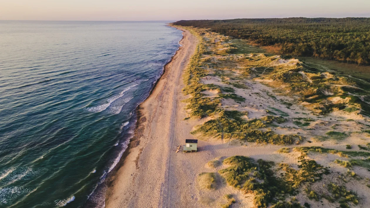 Remote view of Tisvilde Beach, Denmark, with sandy dunes and a small hut along the coast.
