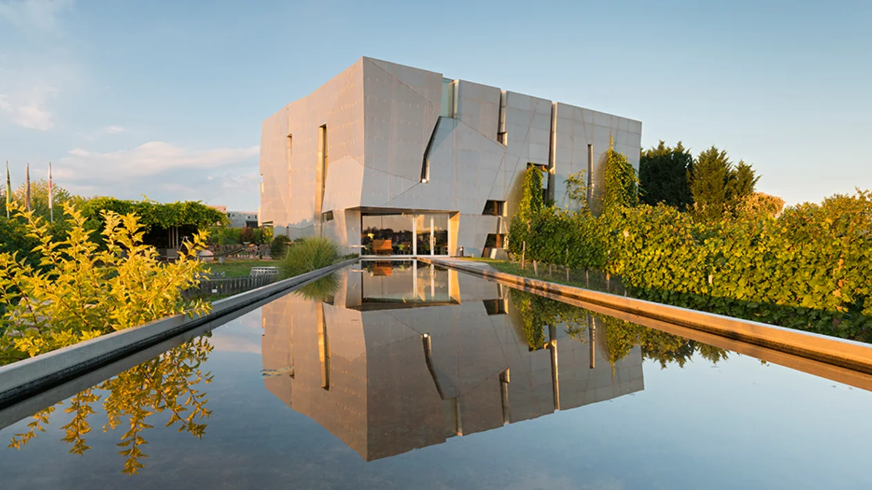 Modern LOISIUM WineWorld building in Austria, designed by architect Steven Holl, with vineyard reflections in the water feature.