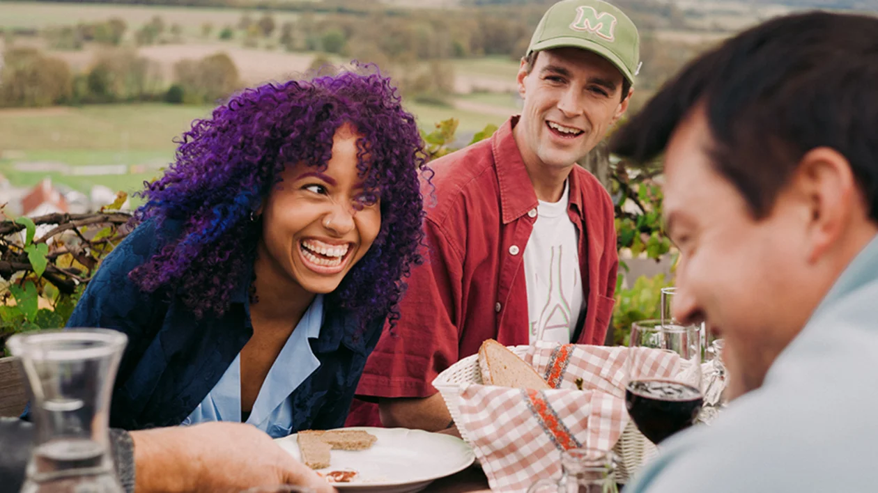 Friends sharing bread, wine, and laughter at a traditional Austrian wine tavern with vineyard views.