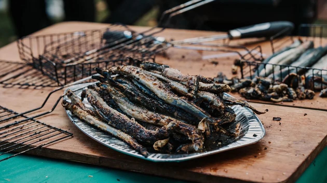 Grilled smelt fish stacked on a plate at the Smelt Festival in Narva-Jõesuu, Estonia, with barbecue racks in the background.