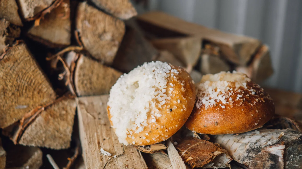 Two golden, soft pastries topped with coarse white sugar sit on wooden logs and rustic foliage.