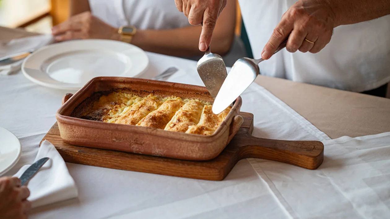 Close-up of traditional Croatian štrukli pastry being served hot from a baking dish at a dining table.