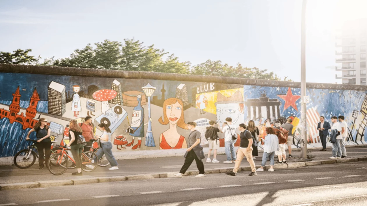 Sunlit East Side Gallery in Berlin with people walking along the open-air mural gallery on a clear day.
