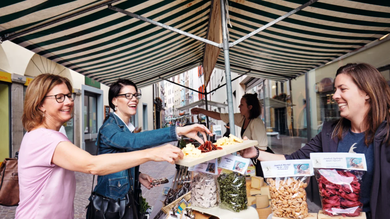 Two women sampling traditional Swiss delicacies at a stall in Chur Market.