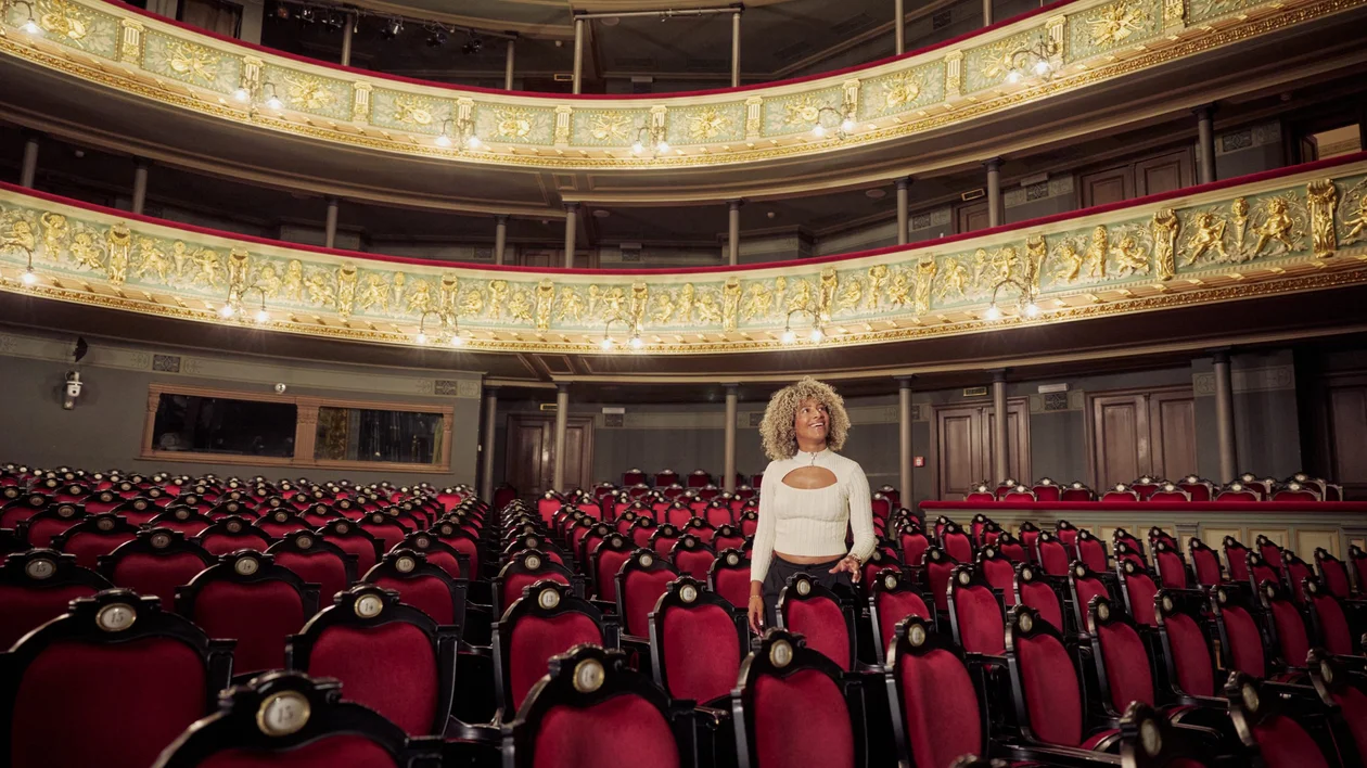 Interior of the Latvian National Opera in Riga, with ornate gold balconies and red velvet seats, viewed from the auditorium.