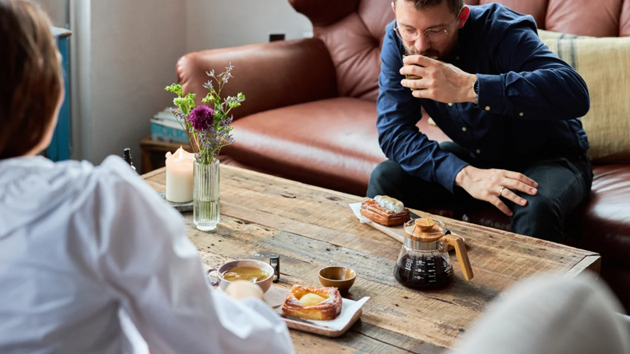 Couple enjoying coffee and Danish pastries in a relaxed café setting with rustic wooden table and natural light.