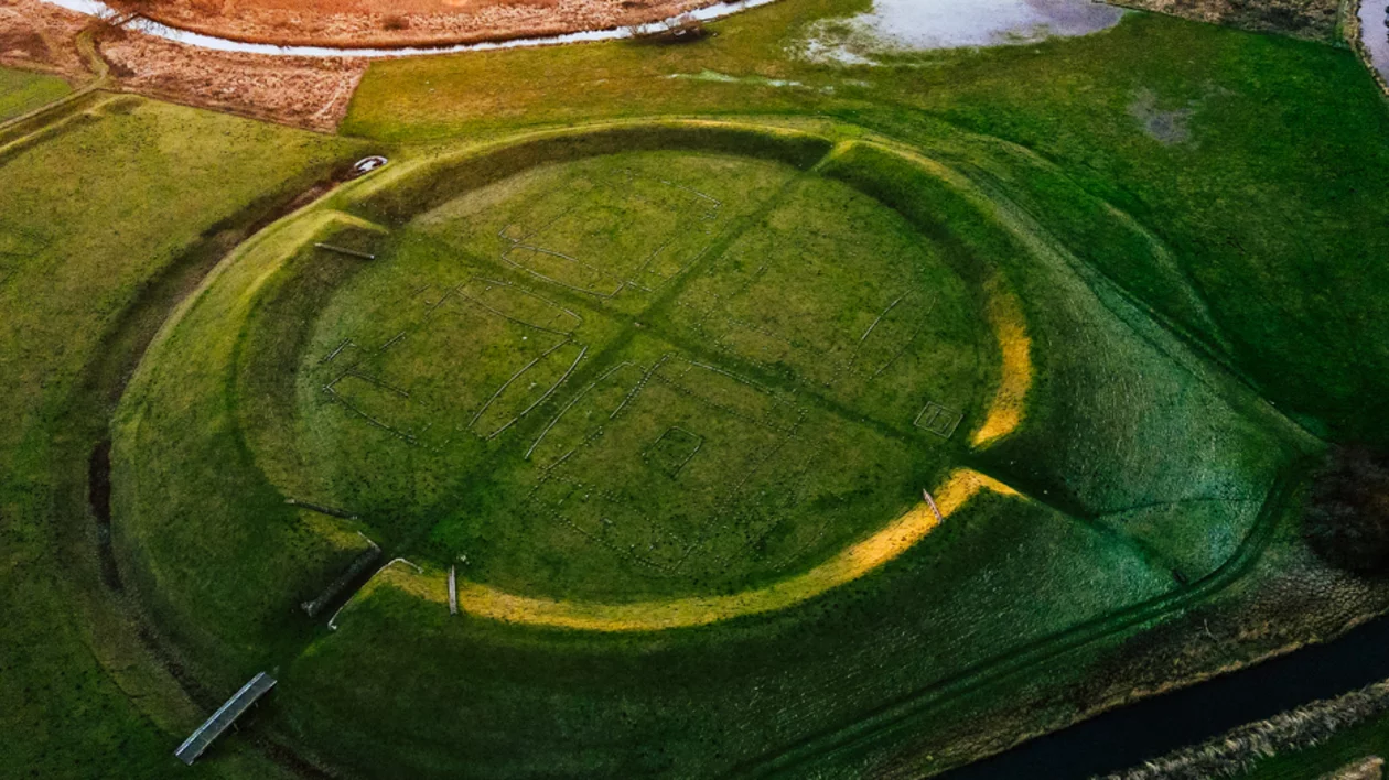 An aerial view of the Trelleborg Viking ring fortress in Denmark, showing its distinct circular earthen ramparts and internal cruciform layout marked on the grassy field.