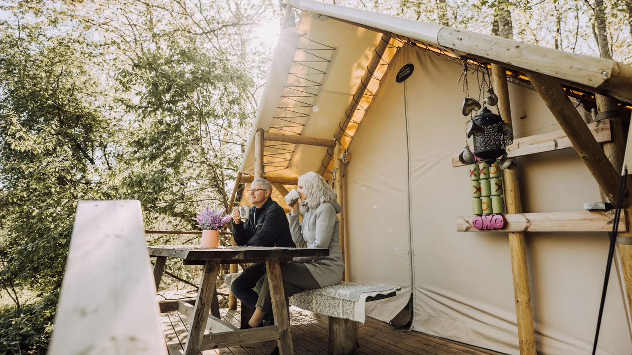 A couple relaxing on the wooden deck of a safari-style tent at a Torma glamping site.