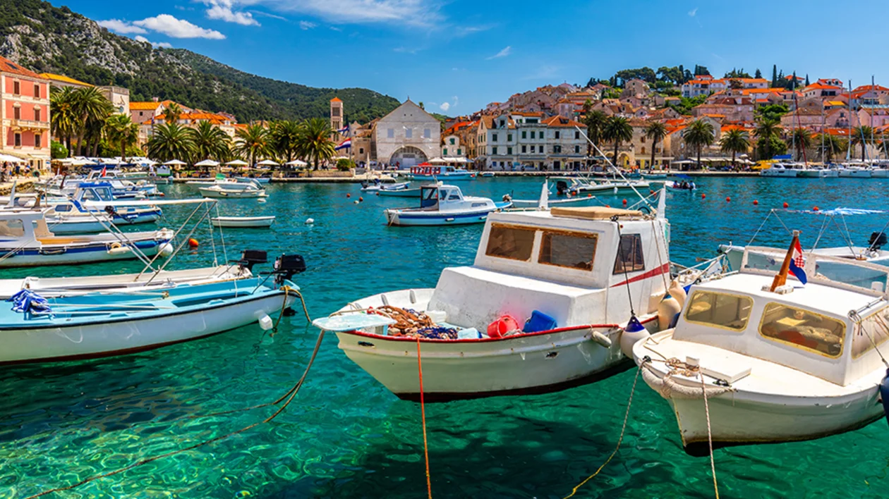 Boats anchored in the turquoise harbour of Hvar Town, Croatia, with historic buildings and palm trees in the background.
