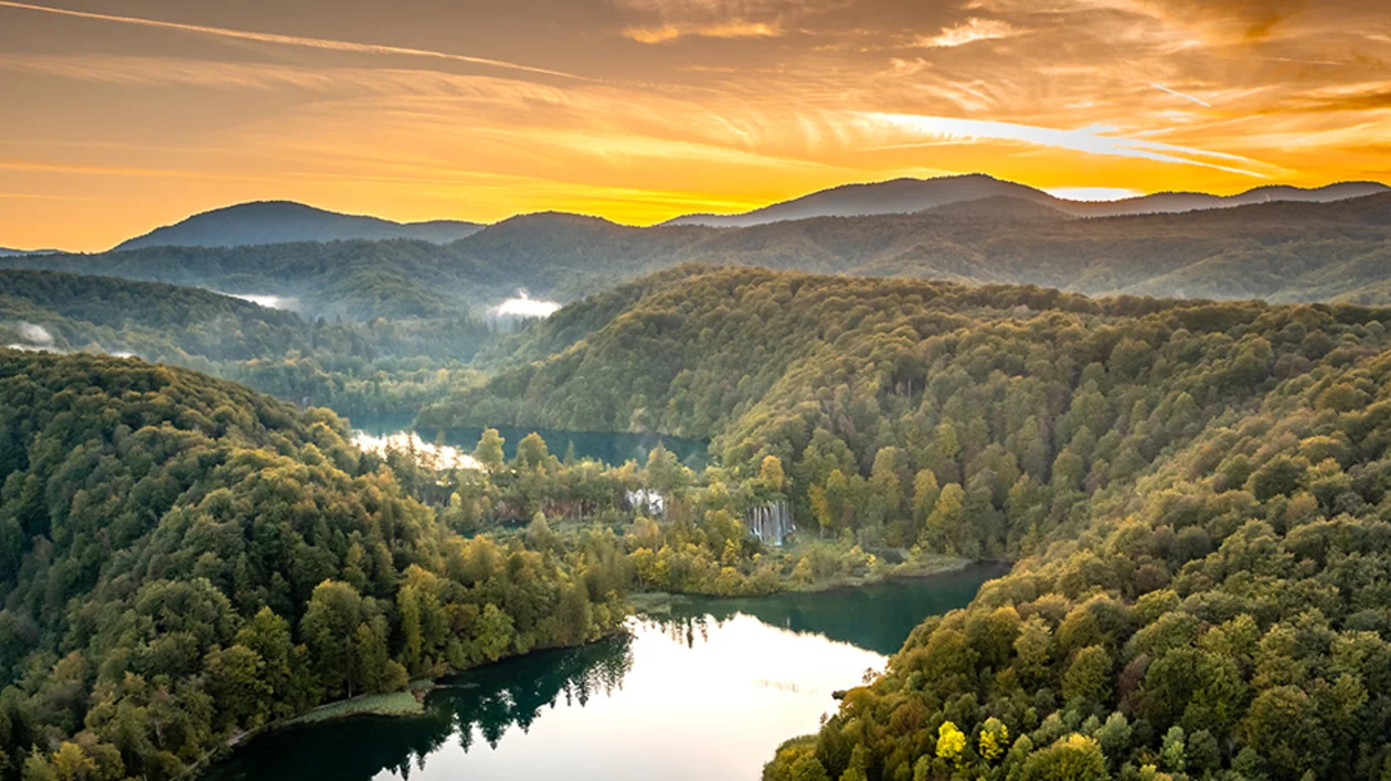 Sweeping sunset view of the forested valleys and turquoise, terraced lakes of Plitvice Lakes National Park in Croatia.