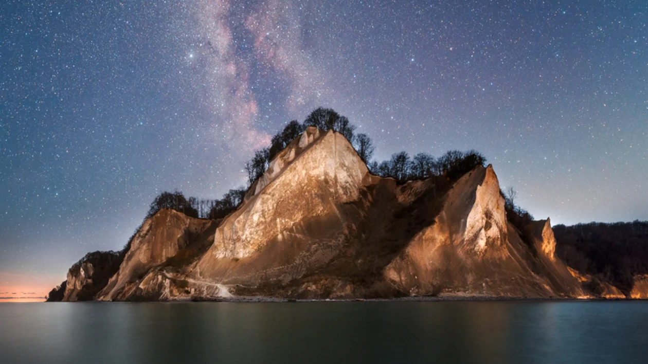 Night sky over the white chalk cliffs of Møns Klint in Denmark, with thousands of stars visible above the Baltic Sea.