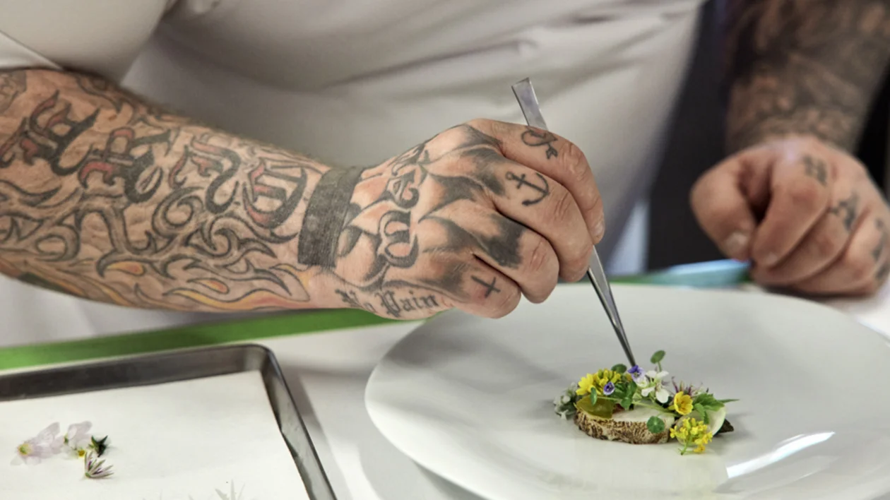 Chef at three‑Michelin‑star restaurant Jordnær in Gentofte, Denmark, plating a delicate dish with edible flowers and microgreens.