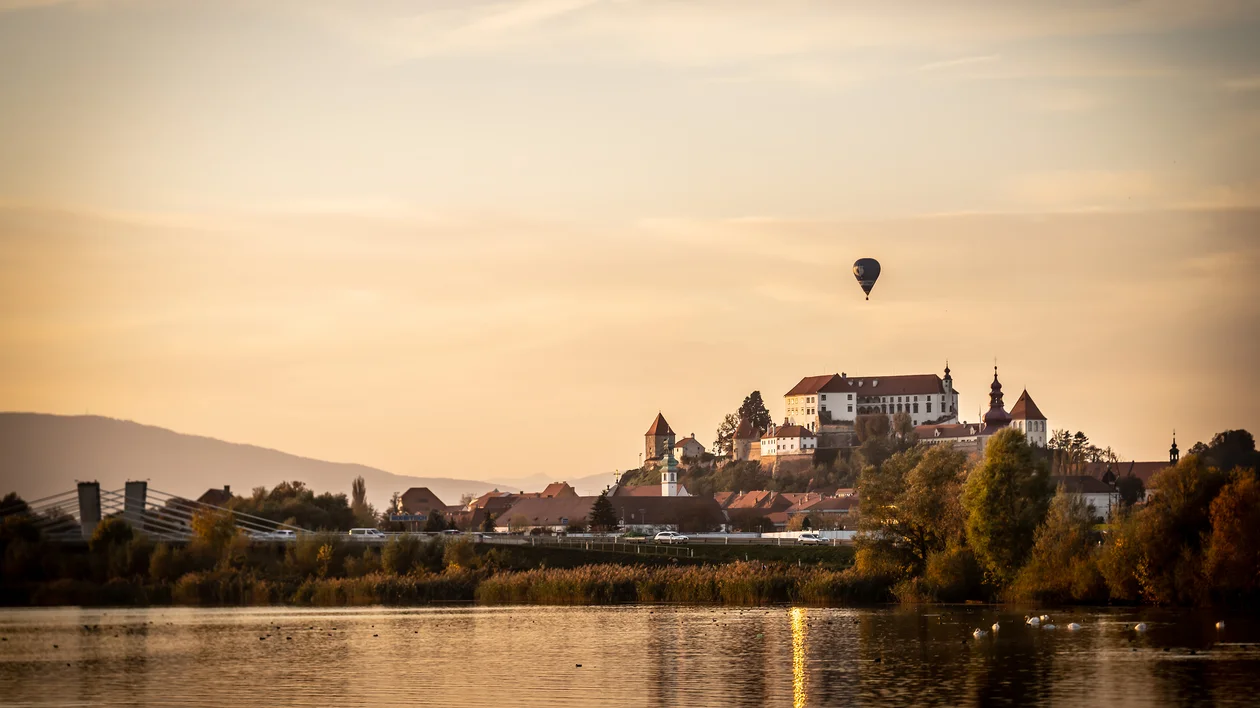 Ptuj Castle overlooking the town at sunset with a hot-air balloon floating above the landscape in Slovenia.