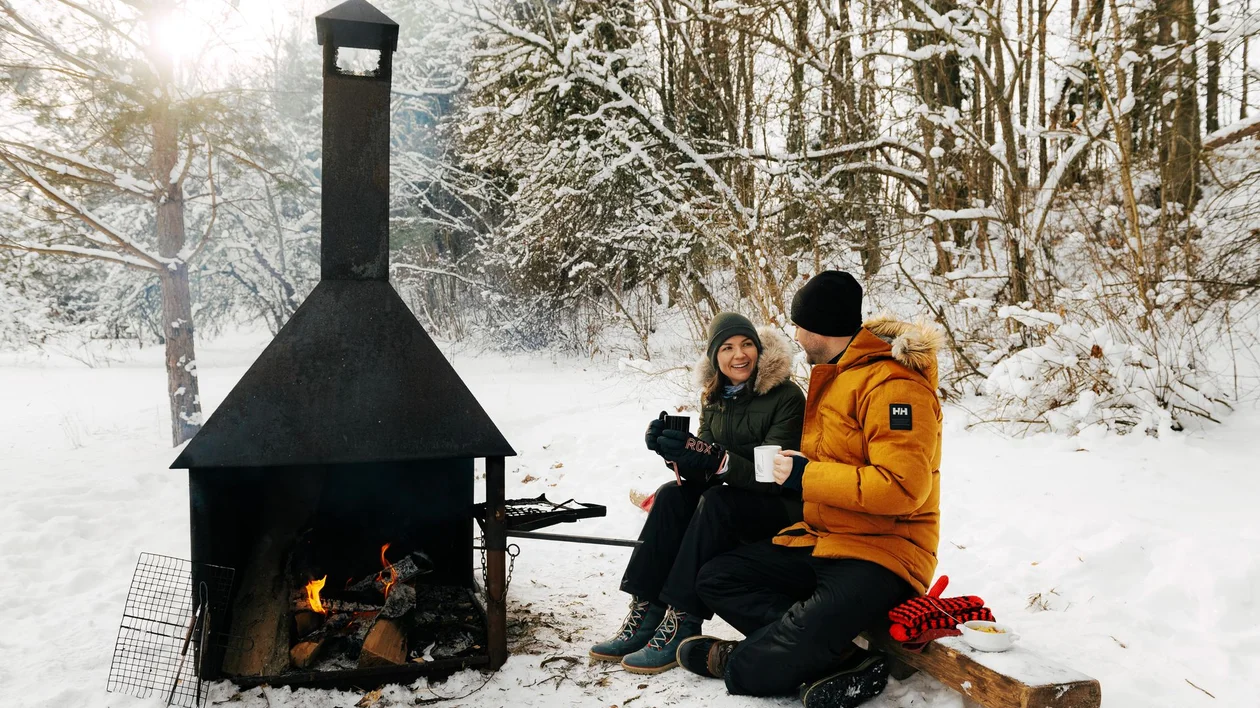Couple warming up by an outdoor fire in a snowy forest.
