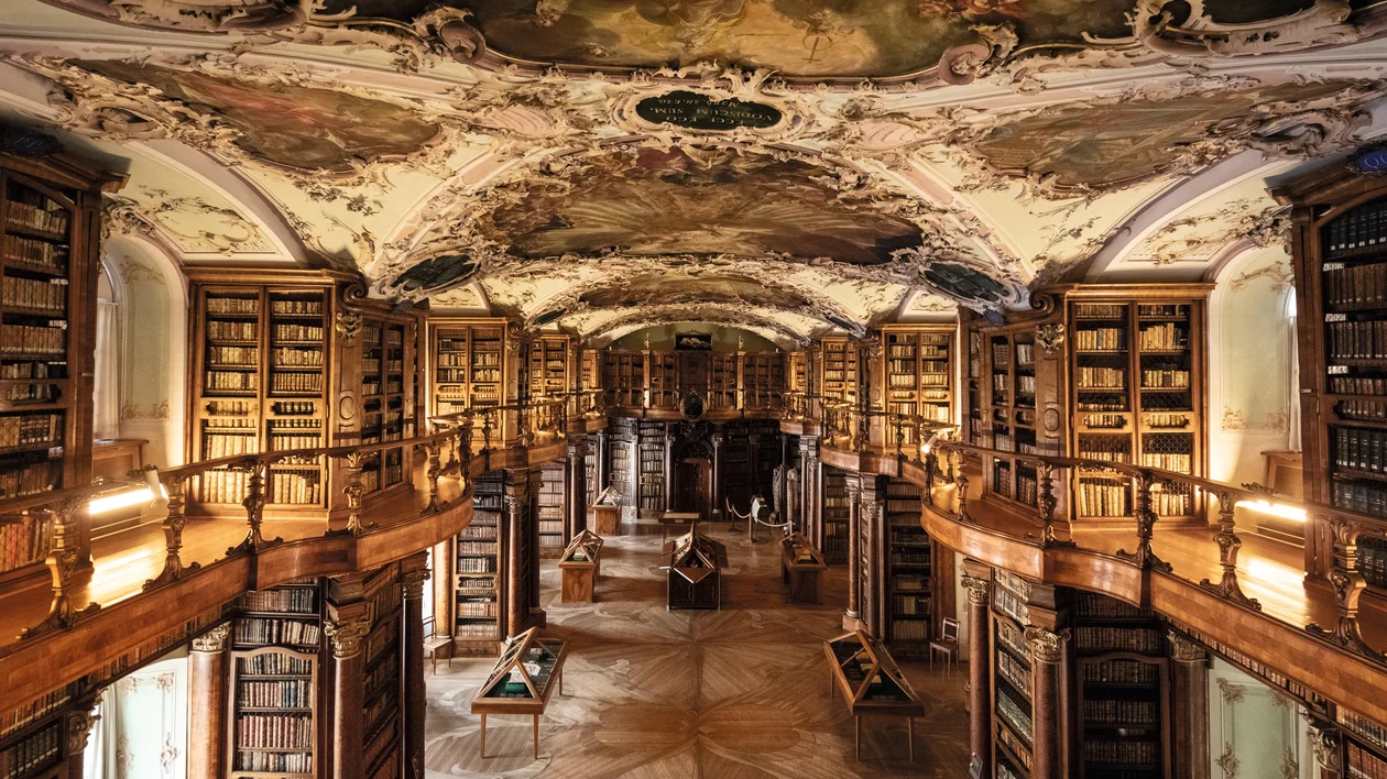 Ornate library with wooden bookshelves, arched ceiling, and painted frescoes.