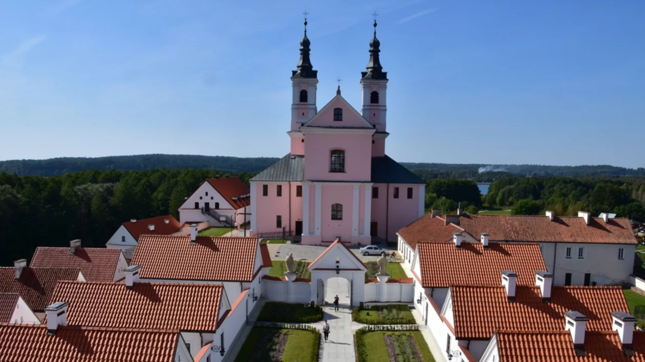 Aerial view of the Camaldolese Monastery in Wigry with pink church towers and red-roofed monastic buildings surrounded by forest