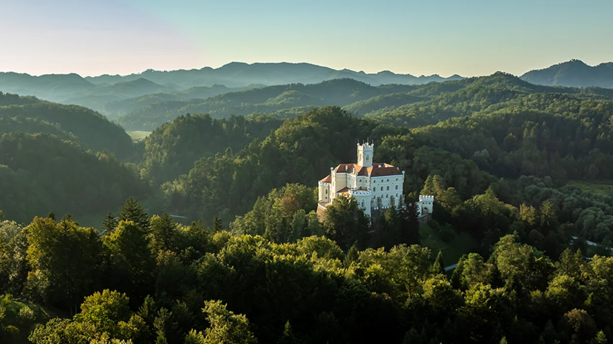 Trakošćan Castle surrounded by forested hills in northern Croatia at sunrise.