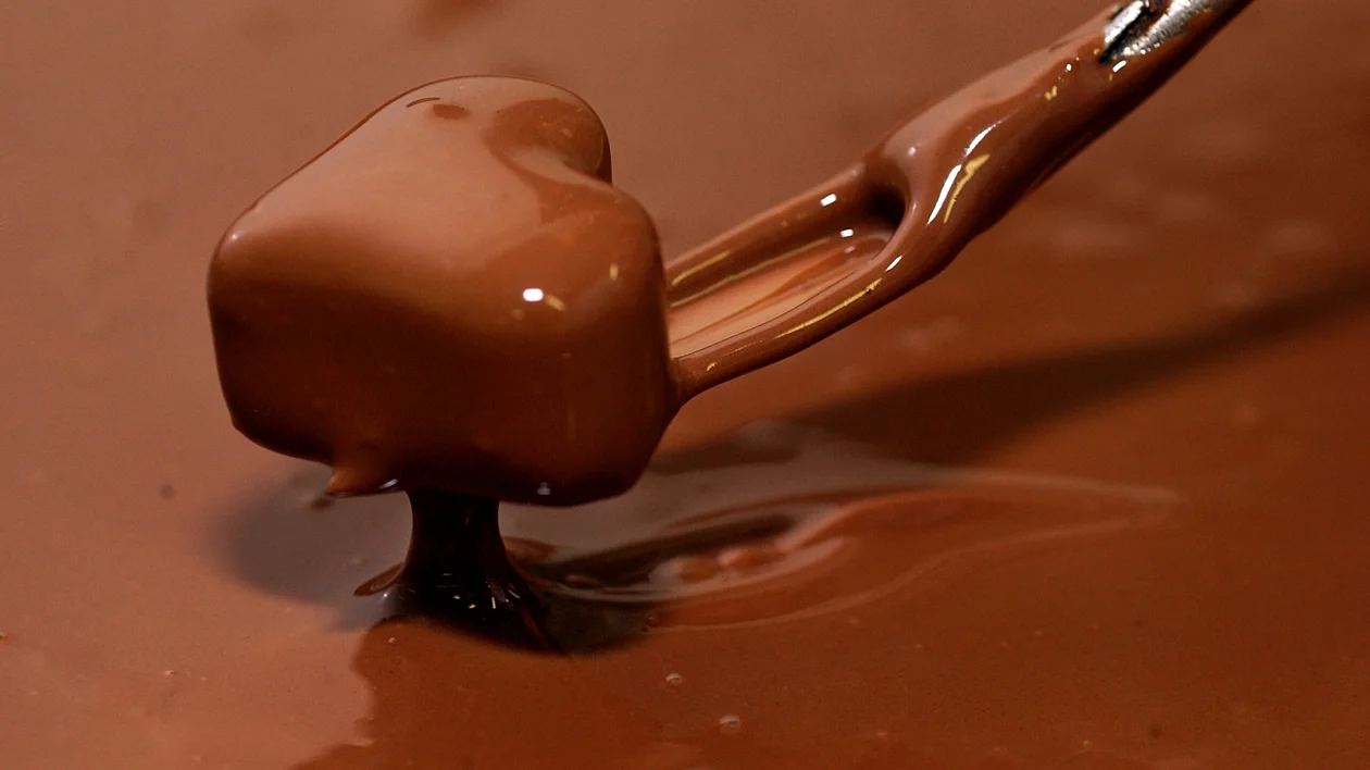 Chocolate praline being dipped in melted chocolate