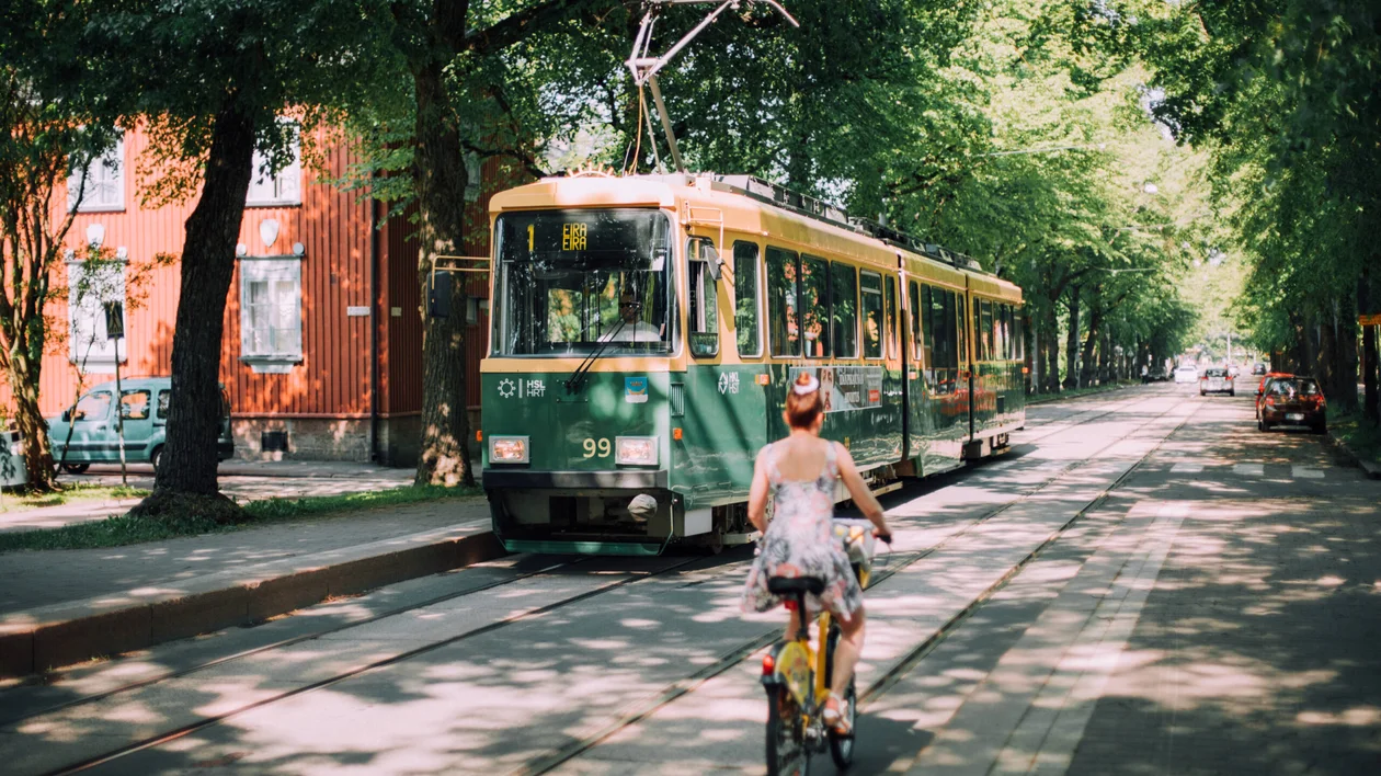 Vintage green tram passing through a tree-lined street with wooden houses in Helsinki, Finland