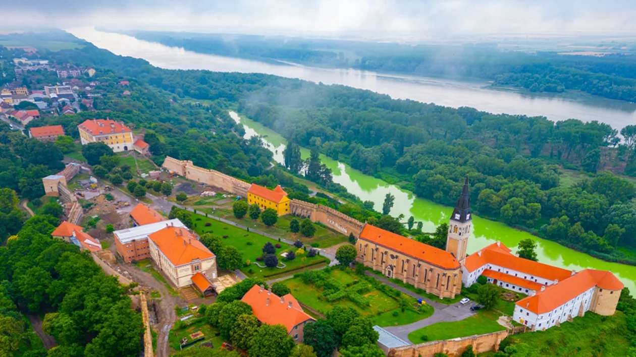 Ilok old town and fortress overlooking the Danube River, surrounded by greenery and vineyards.