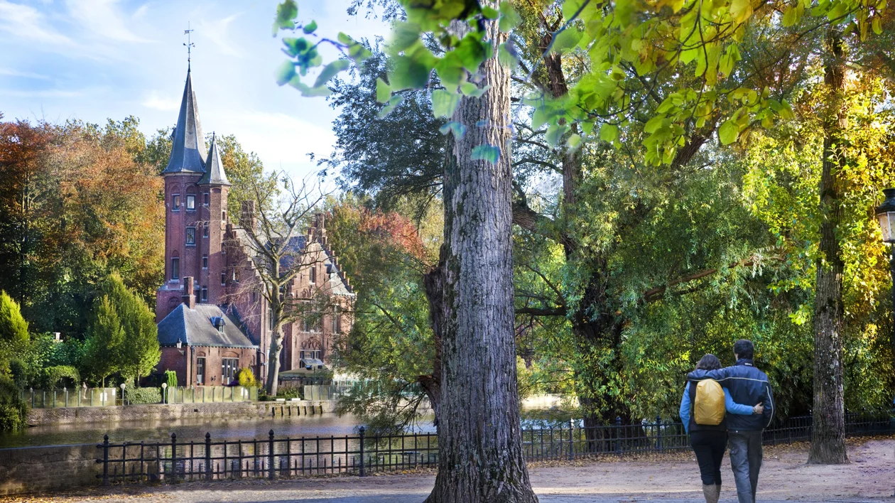 Couple walking beside Minnewater Lake in Bruges, Belgium in autumn.