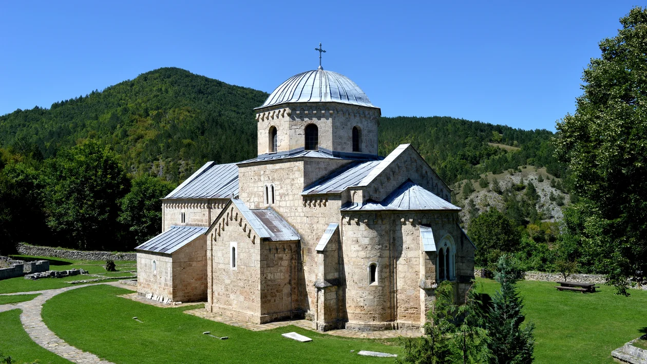 Stone church with a dome surrounded by green grass and trees under a clear blue sky.